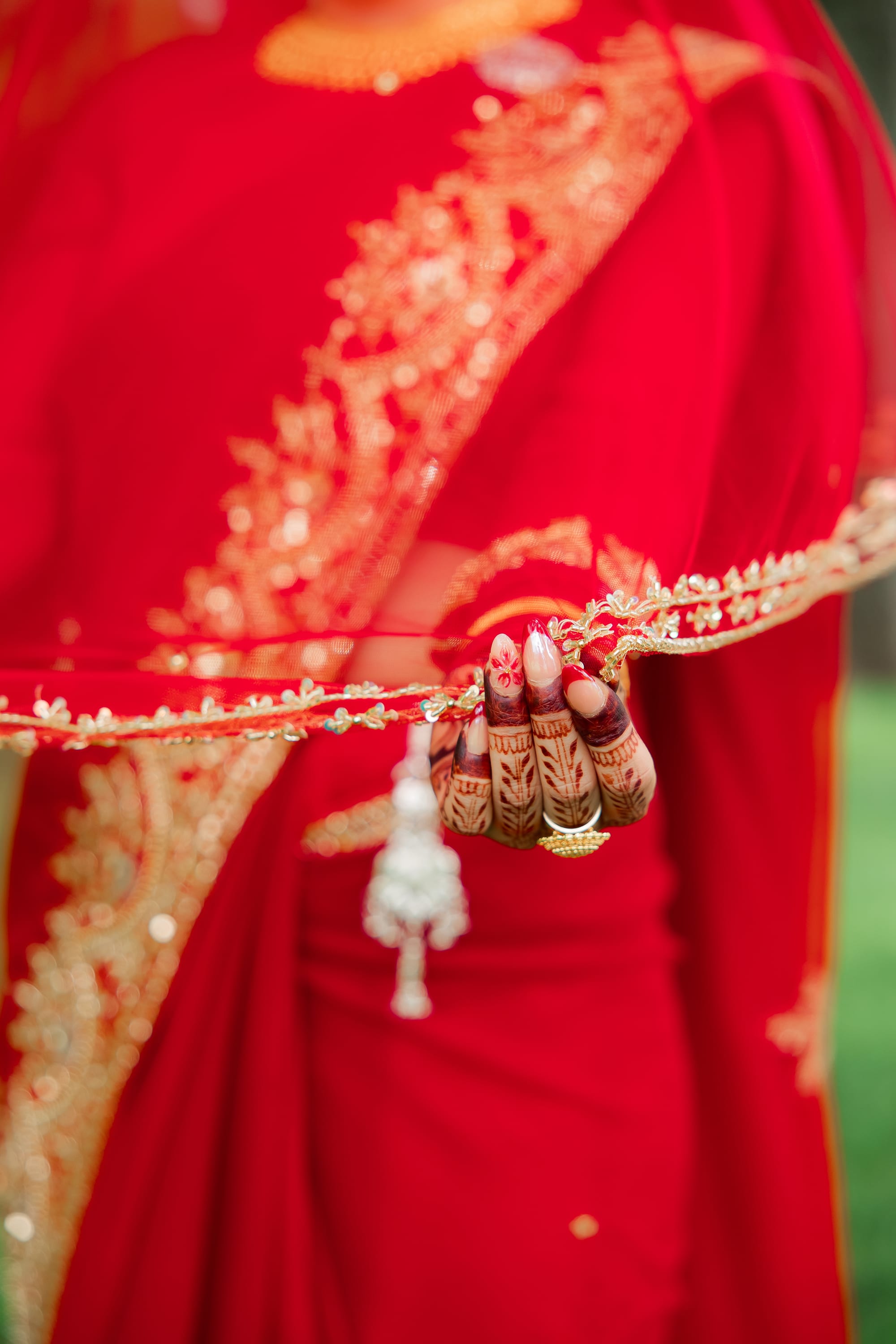 Close-up of a bride's henna-decorated hand holding the gold-trimmed edge of her red saree.