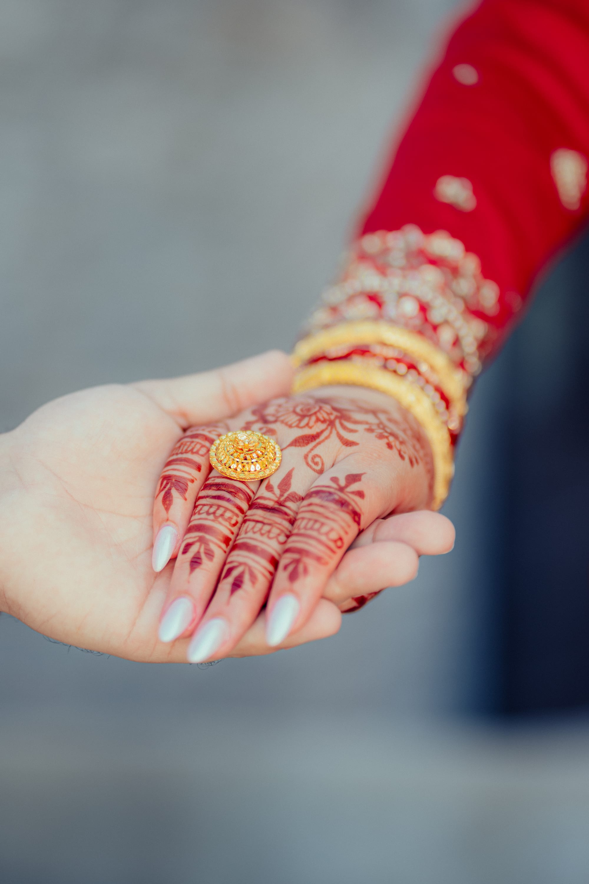 Close-up of joined hands, one hennaed and reaching to place a gold ring in the other's palm.